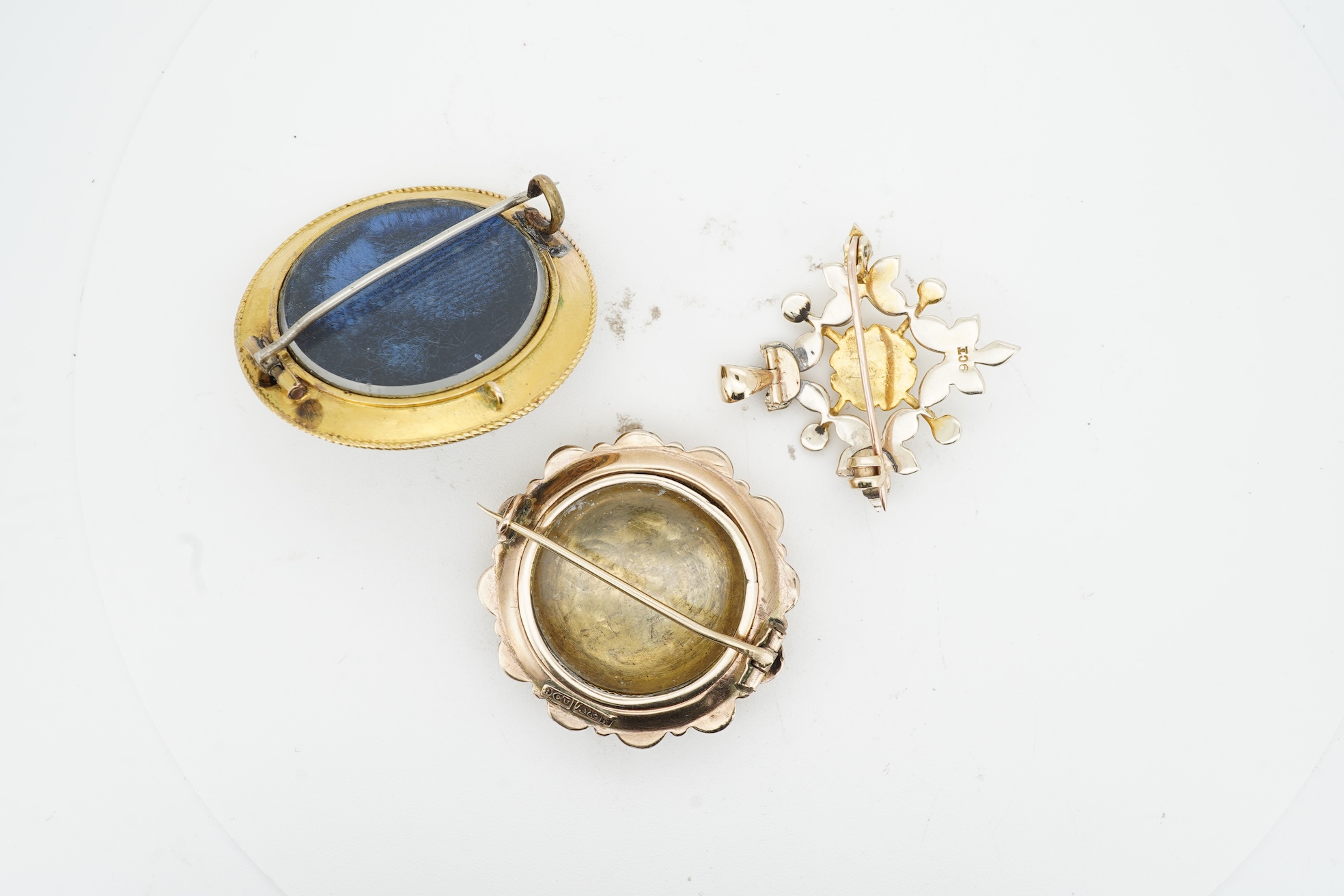 Three brooches, comprising: a Victorian circular brooch centring on a cabochon onyx set with a rose-cut diamond in a star setting, to concentring bands of seed pearls and Greek key motifs in black enamel, the reverse wit
